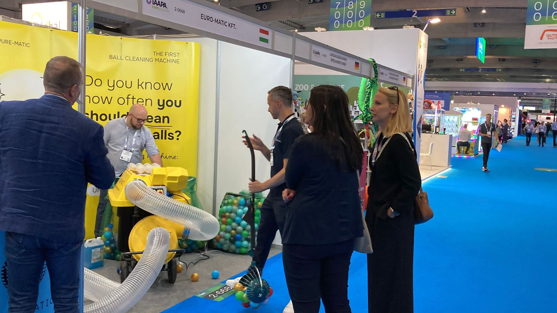 Euro-Matic präsentiert auf der IAAPA Expo Europe 2025 die Ballreinigungsmaschine am Messestand. Besucher verfolgen die Demonstration der Reinigung von Spielbällen.