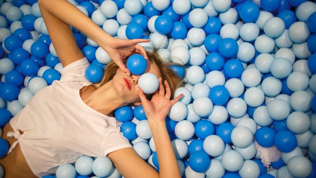 Bällebad für Erwachsene, Frau liegt im Bällebad und hält sich zwei Bällebad Kugeln vor die Augen